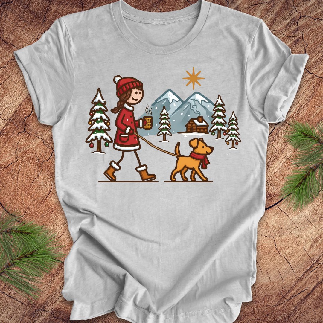 Gray t-shirt with a graphic of a person walking a dog in a winter landscape on a wooden surface.