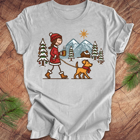 Gray t-shirt with a graphic of a person walking a dog in a winter landscape on a wooden surface.