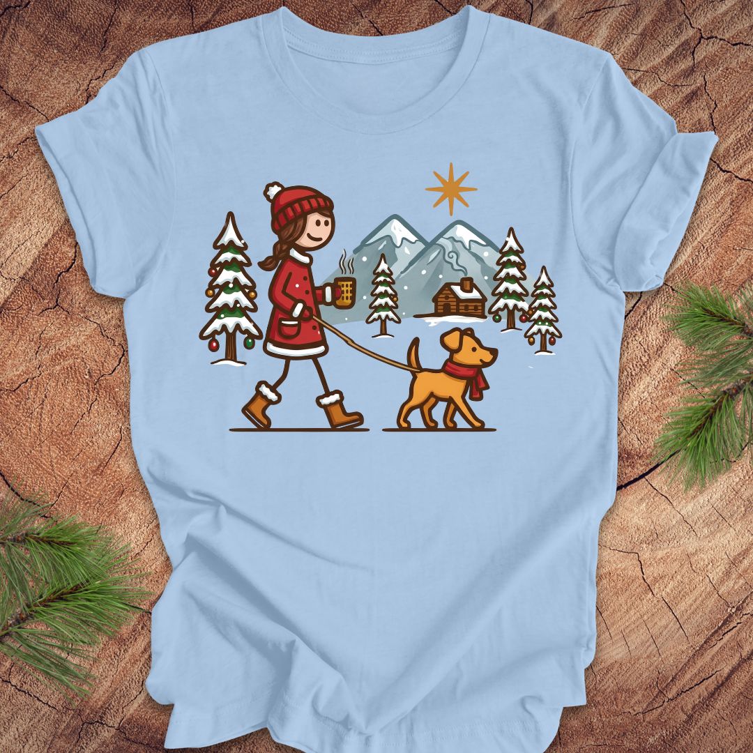 Light blue t-shirt with a graphic of a person walking a dog in a winter landscape on a wooden surface.