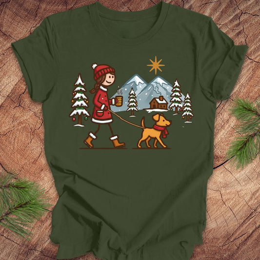 Green t-shirt with a winter scene design featuring a person and dog on a leash, placed on a wooden surface.
