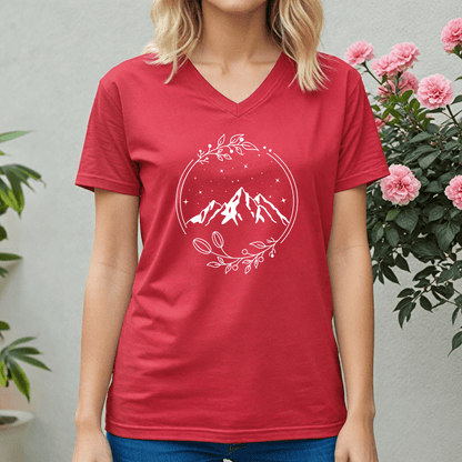 Person wearing a red t-shirt with a mountain design, standing in front of pink flowers and green plants.