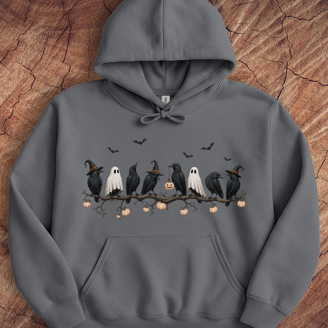 A dark gray pullover hoodie featuring a Halloween-themed graphic print of black crows, white ghosts, and pumpkins on a branch, displayed flat against a textured wood background.