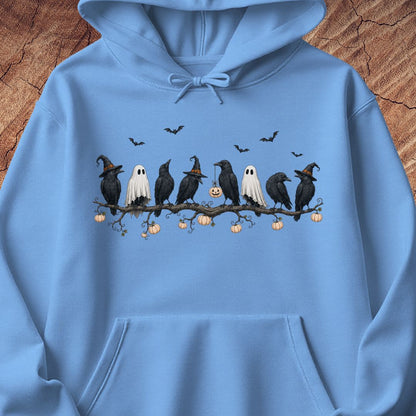 A light blue hoodie laid flat on a rustic wood background, featuring a Halloween graphic of black crows, white ghosts, and small pumpkins on a branch across the chest.