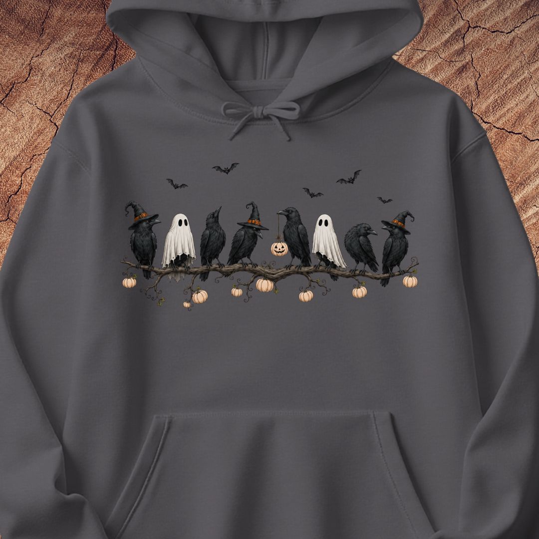 A dark gray hoodie featuring a Halloween graphic print of black crows, white ghosts, and a jack-o'-lantern on a branch, displayed against a rustic wood background.