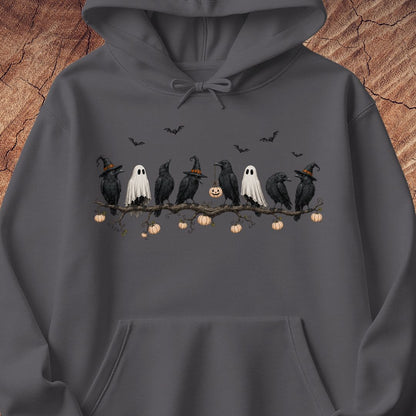 A dark gray hoodie featuring a Halloween graphic print of black crows, white ghosts, and a jack-o'-lantern on a branch, displayed against a rustic wood background.