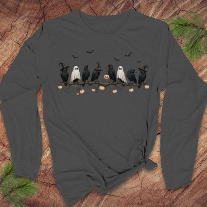 A dark gray long-sleeve t-shirt with a Halloween graphic of crows, ghosts, and pumpkins, laid flat on a rustic wood background with pine needles.