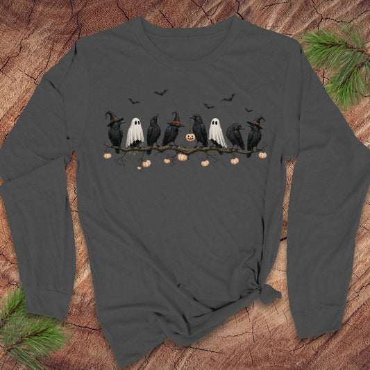 A dark gray long-sleeve t-shirt with a Halloween graphic of crows, ghosts, and pumpkins, laid flat on a rustic wood background with pine needles.