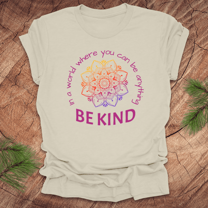 Beige t-shirt with a colorful mandala and 'BE KIND' text on a wooden surface.
