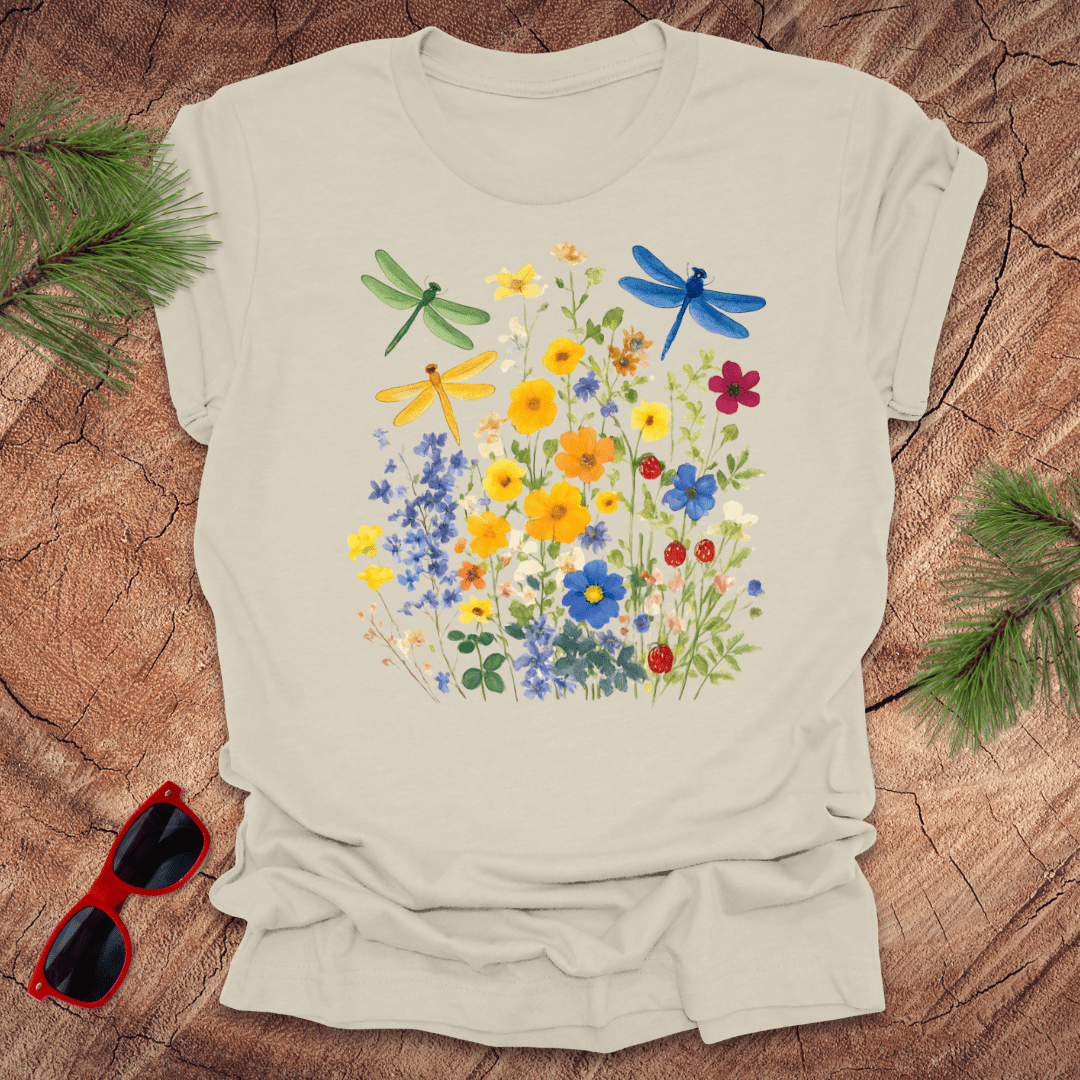 Beige t-shirt with floral and dragonfly design on a wooden surface with sunglasses and greenery.