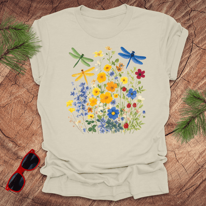Beige t-shirt with floral and dragonfly design on a wooden surface with sunglasses and greenery.