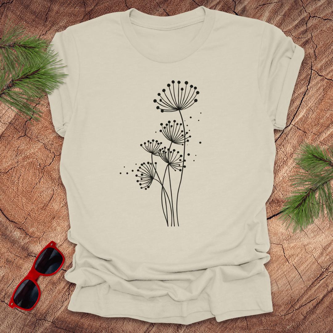 Beige t-shirt with black floral dandelion design on a wooden surface with sunglasses and greenery.