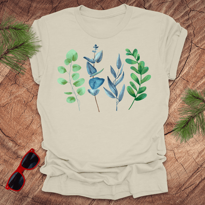 Beige t-shirt with leaf design on a wooden surface with sunglasses and greenery.