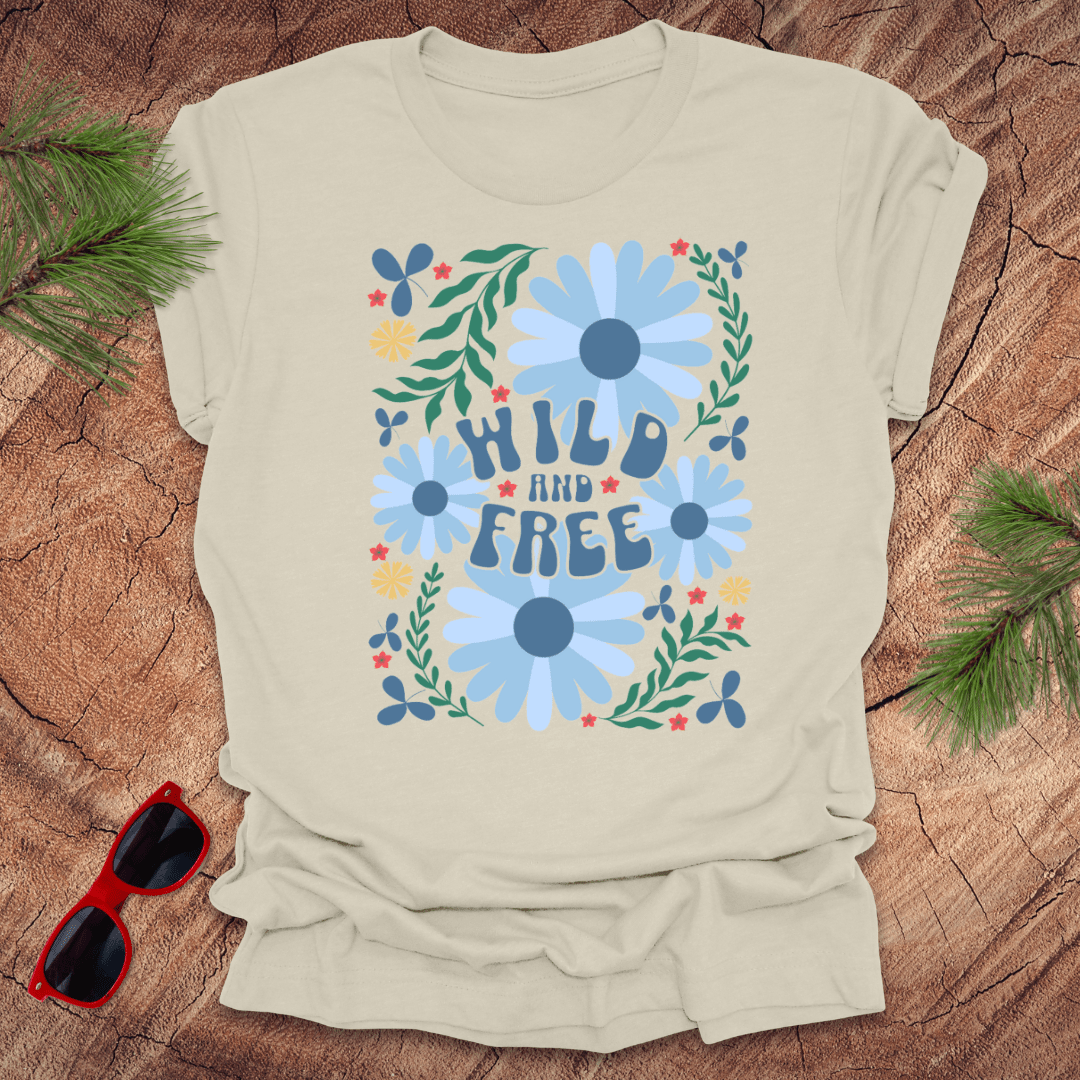 Beige t-shirt with floral design and 'Wild and Free' text on a wooden surface with sunglasses and greenery.