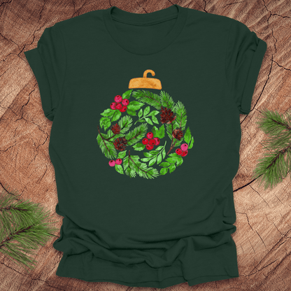 Green t-shirt with a Christmas ornament design featuring greenery and berries on a wooden surface.