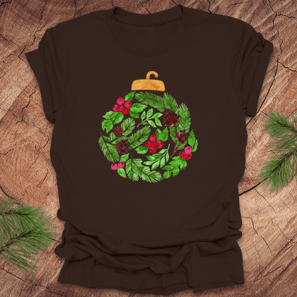 Brown t-shirt with a Christmas ornament design featuring green leaves and red berries on a wooden surface.