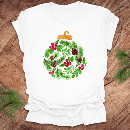 White t-shirt with a Christmas ornament design featuring greenery and berries on a wooden surface.