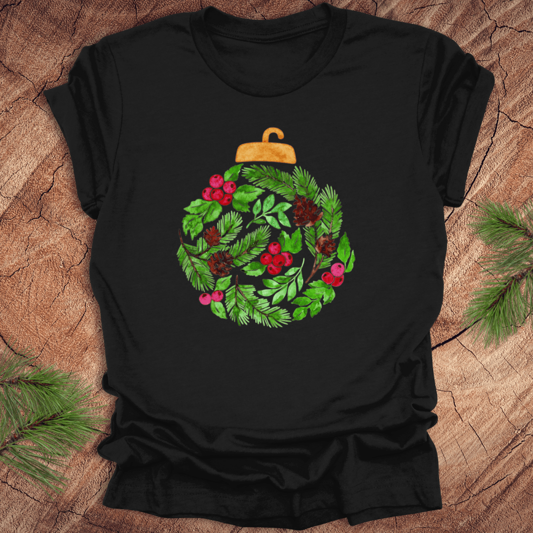 Black t-shirt with a Christmas ornament design featuring green leaves and red berries on a wooden surface.