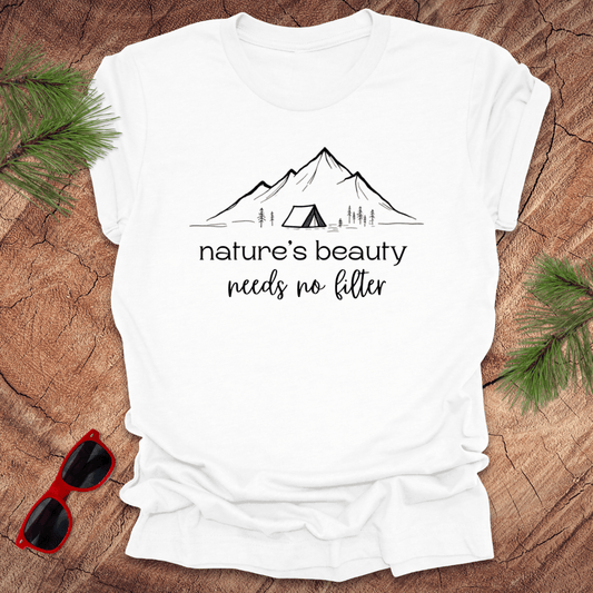 White tshirt with mountains and tent graphic with text, 'nature's beauty needs no filter' on a wood background.