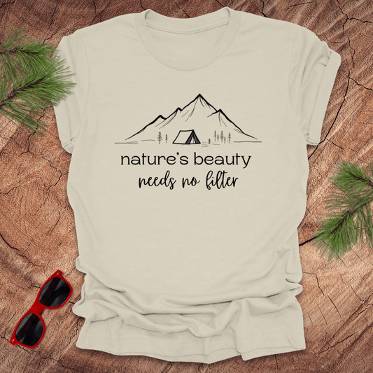 Beige tshirt with mountains and tent graphic with text, 'nature's beauty needs no filter' on a wood background.