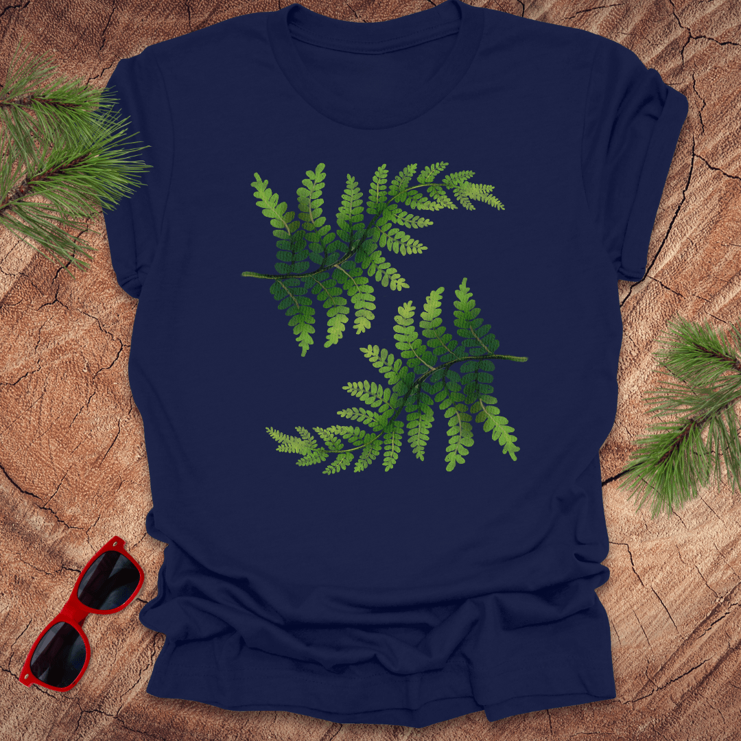Navy blue t-shirt with green leaf design on a wooden surface with sunglasses and pine branches.