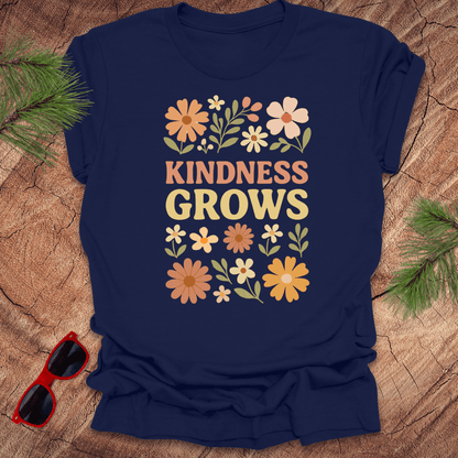 Navy blue t-shirt with flowers and text 'Kindness Grows' on a wood background.