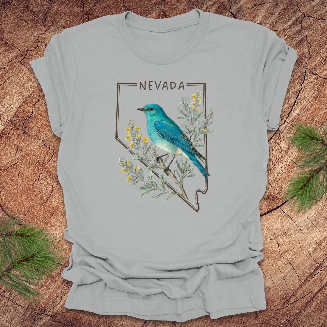 Silver t-shirt with Nevada state design featuring a mountain bluebird and sagebrush on a wooden surface.