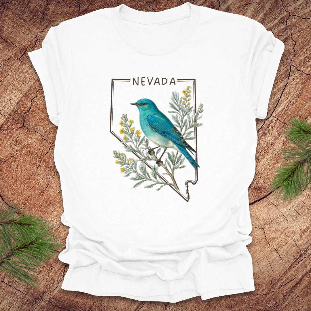 White t-shirt with Nevada state design featuring a mountain bluebird and sagebrush on a wooden surface.