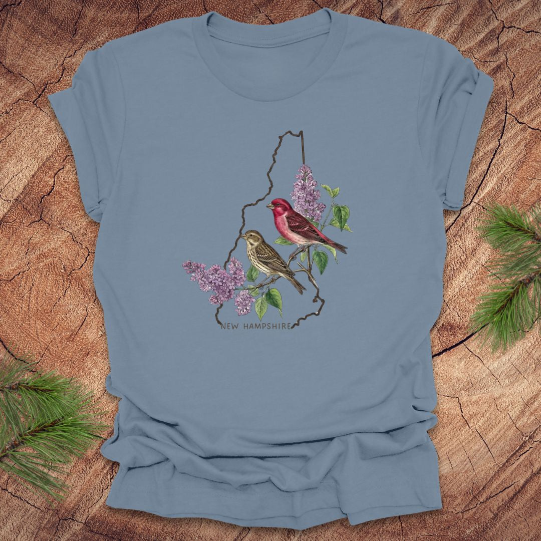 Steel blue t-shirt with New Hampshire design featuring purple finches and purple lilac on a wooden surface.