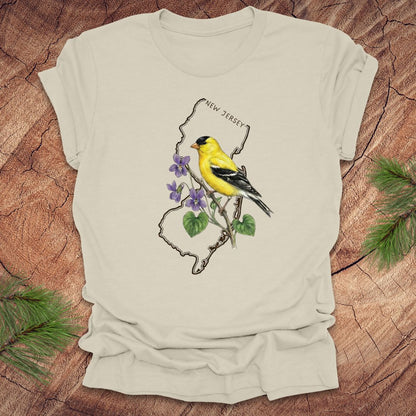 Beige t-shirt with a goldfinch and violets in a New Jersey state outline design on a wooden surface