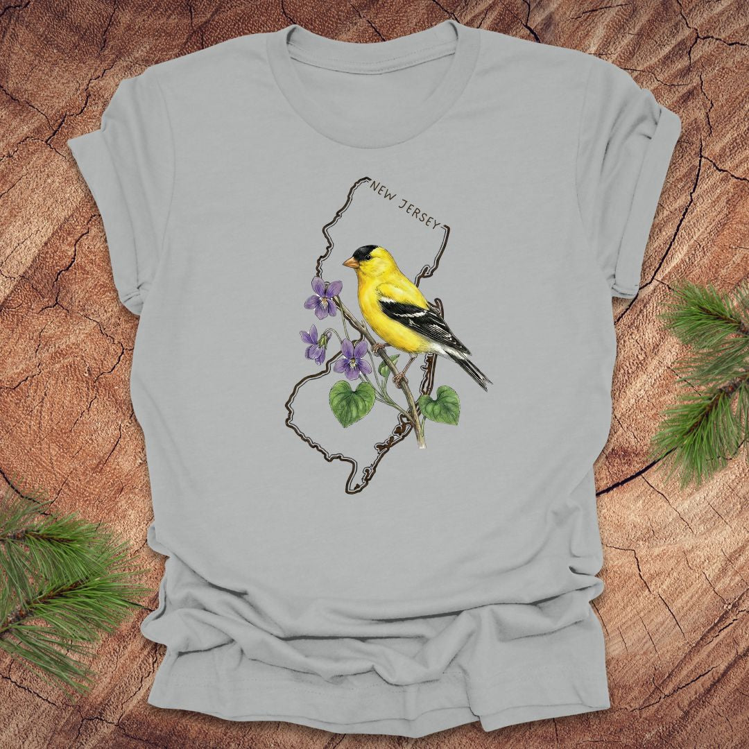 Silver t-shirt with a goldfinch and violets in a New Jersey state outline design on a wooden surface