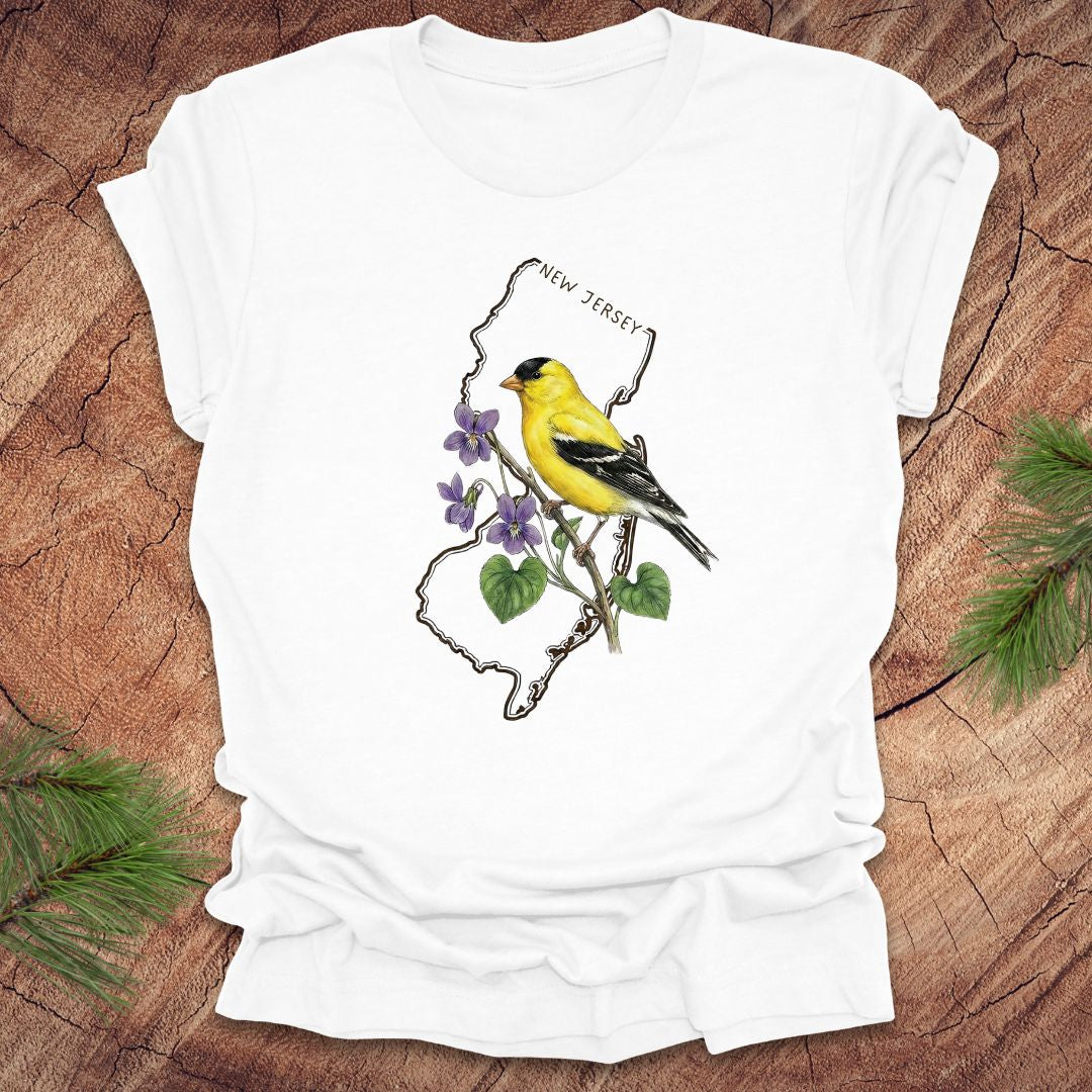 White t-shirt with a goldfinch and violets in a New Jersey state outline design on a wooden surface