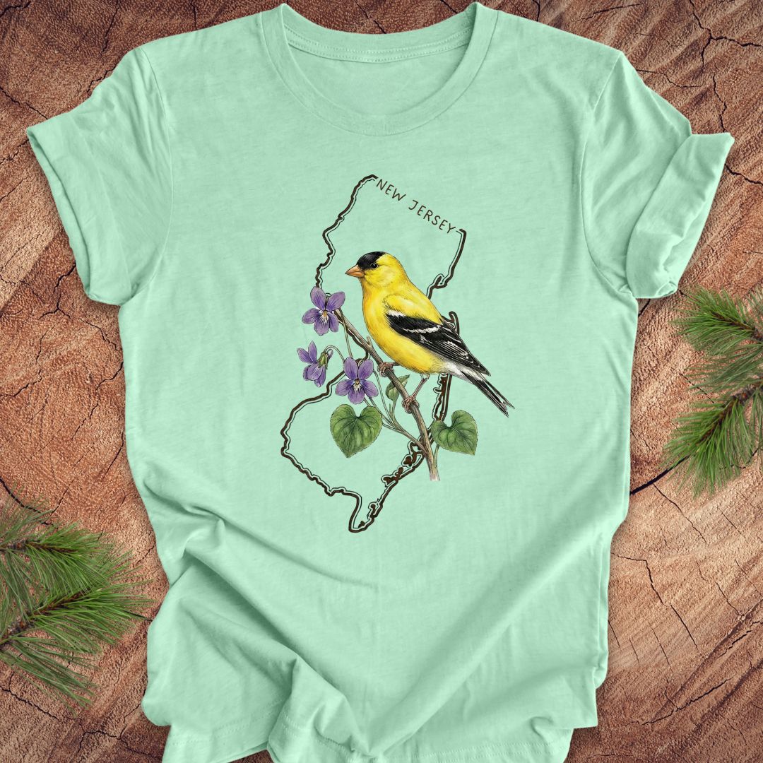 Mint green t-shirt with a goldfinch and violets in a New Jersey state outline design on a wooden surface