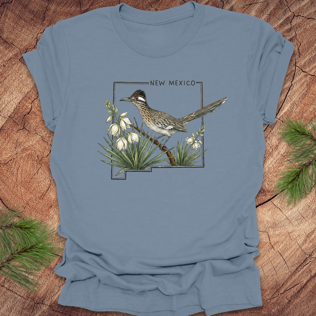 Steel blue t-shirt with outline of state of New Mexico with state bird, roadrunner and flower yucca, on a wooden surface.
