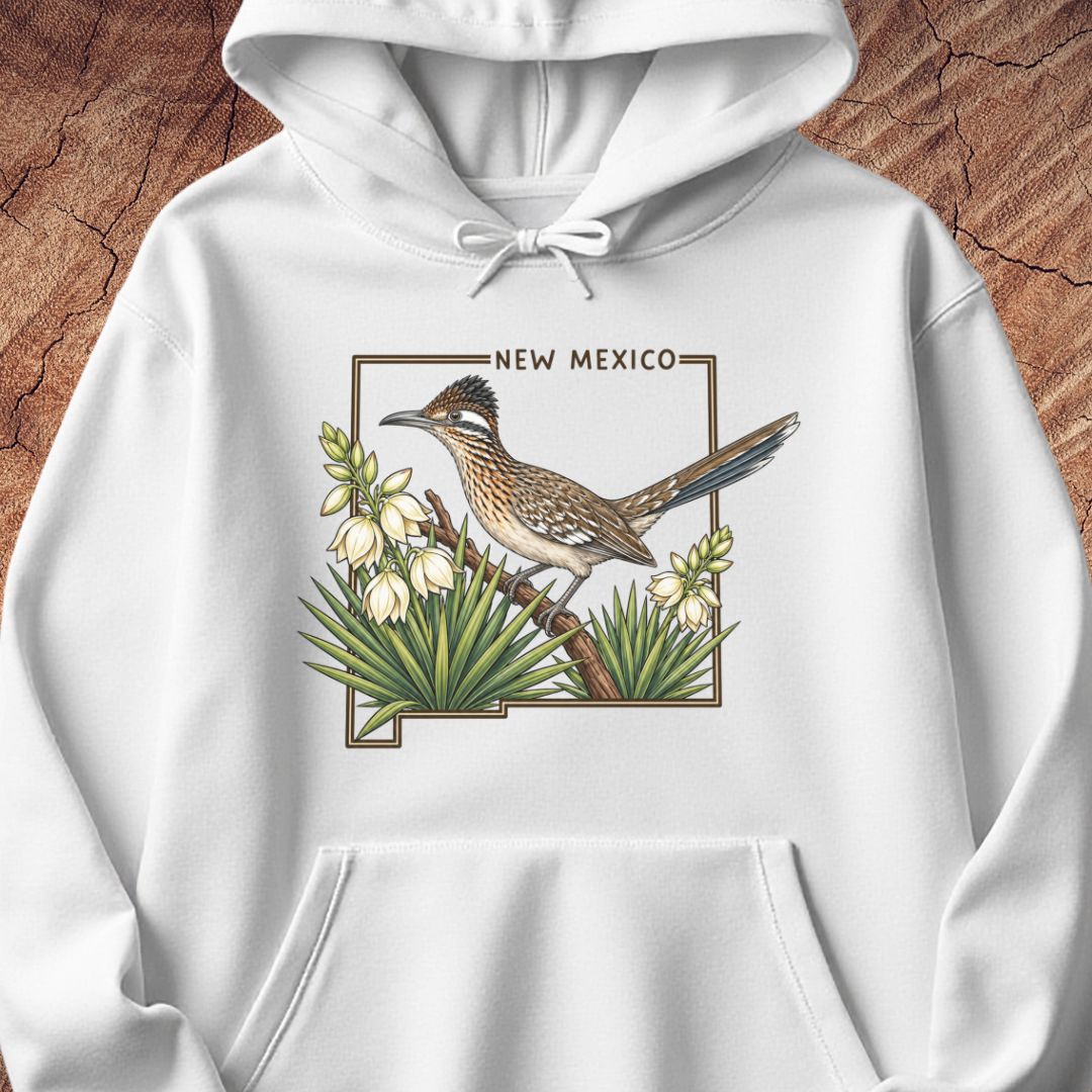 A white pullover hoodie featuring a vintage-style graphic of a roadrunner bird perched on a branch with white flowers, framed by the text 'NEW MEXICO' at the top, shown against a rustic wood background.