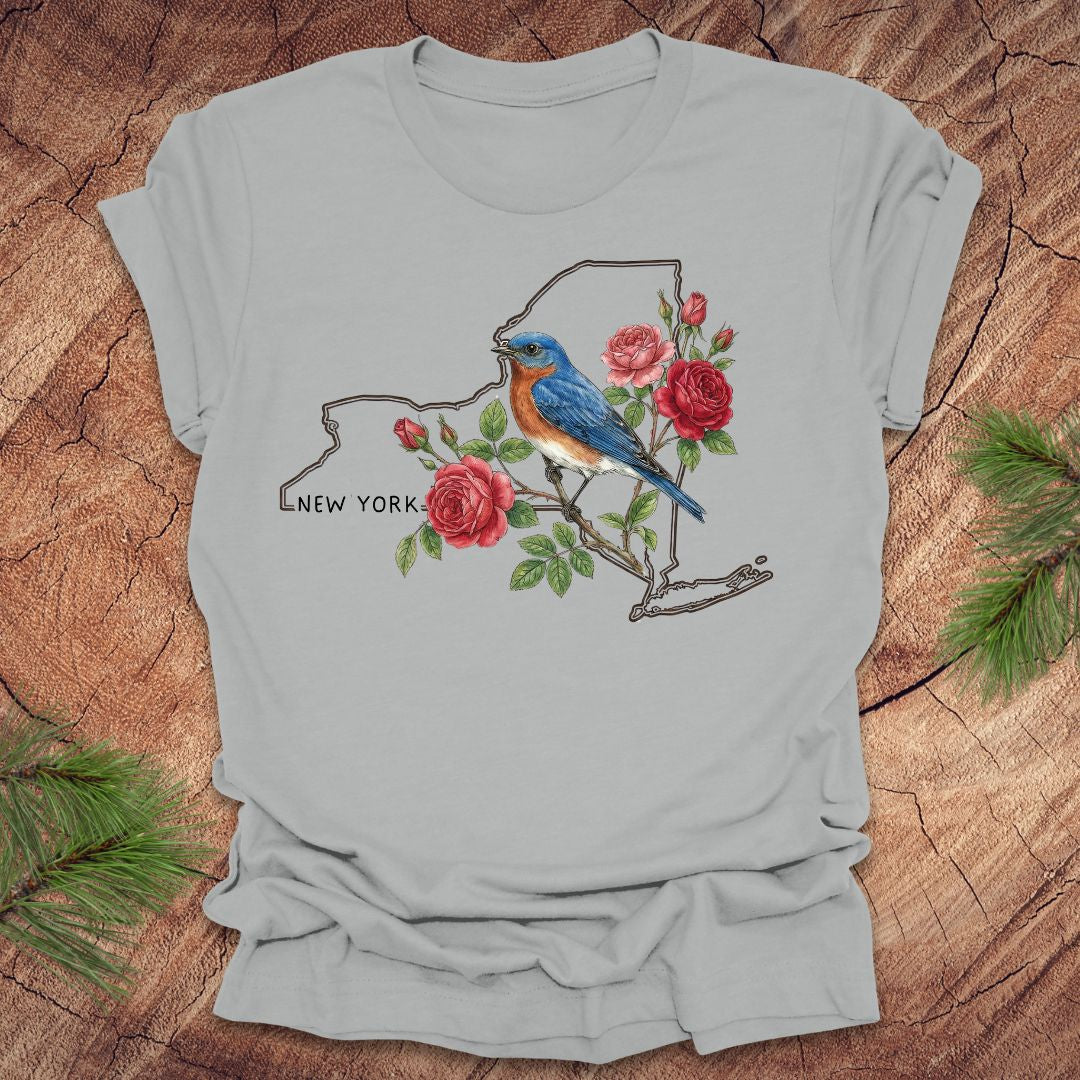 Silver t-shirt with a New York state outline featuring a bluebird and roses on a wooden surface.