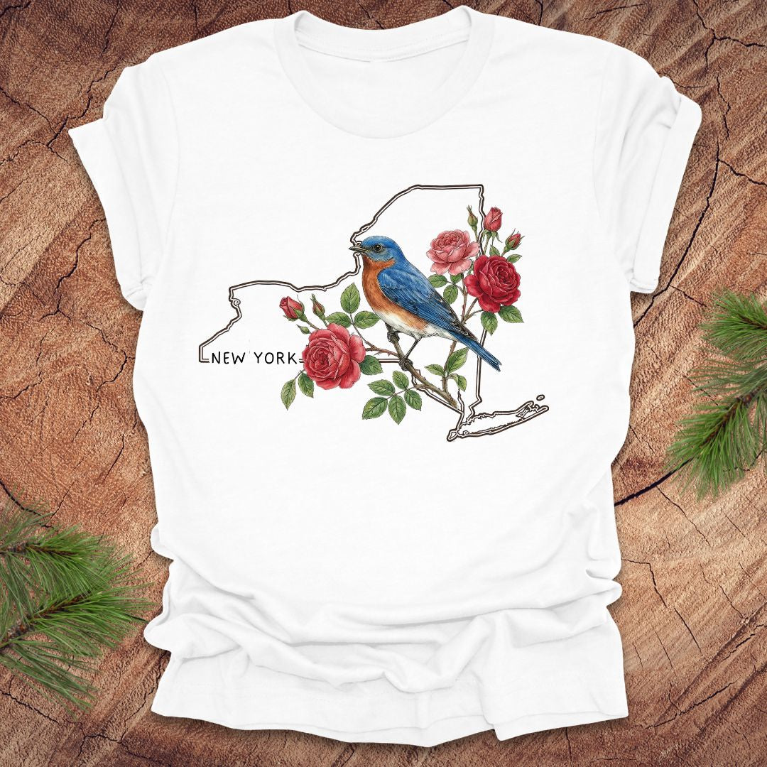 White t-shirt with a New York state outline featuring a bluebird and roses on a wooden surface.
