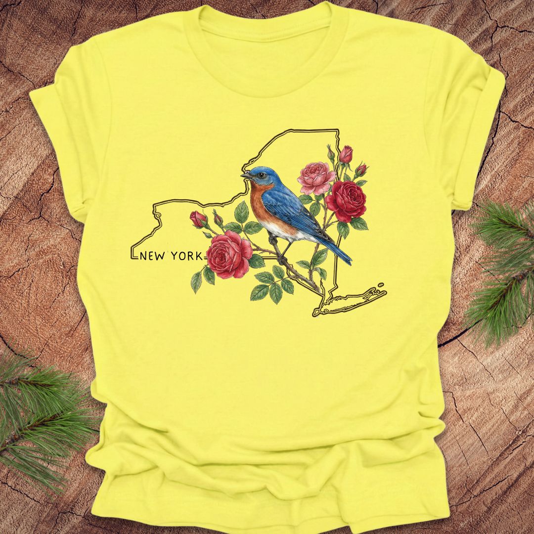 Yellow t-shirt with a bluebird and floral design on New York state outline, placed on a wooden surface.