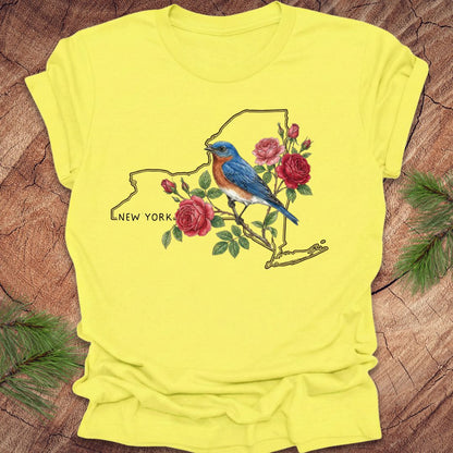 Yellow t-shirt with a bluebird and floral design on New York state outline, placed on a wooden surface.
