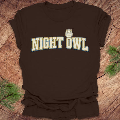 Brown t-shirt with 'NIGHT OWL' text and owl graphic on a wooden surface.