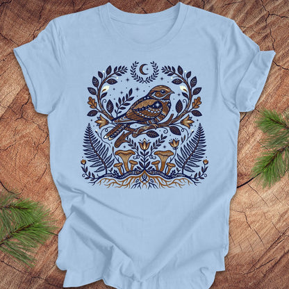 Light blue t-shirt with a whip-poor-will and nature-themed design on a wooden surface.