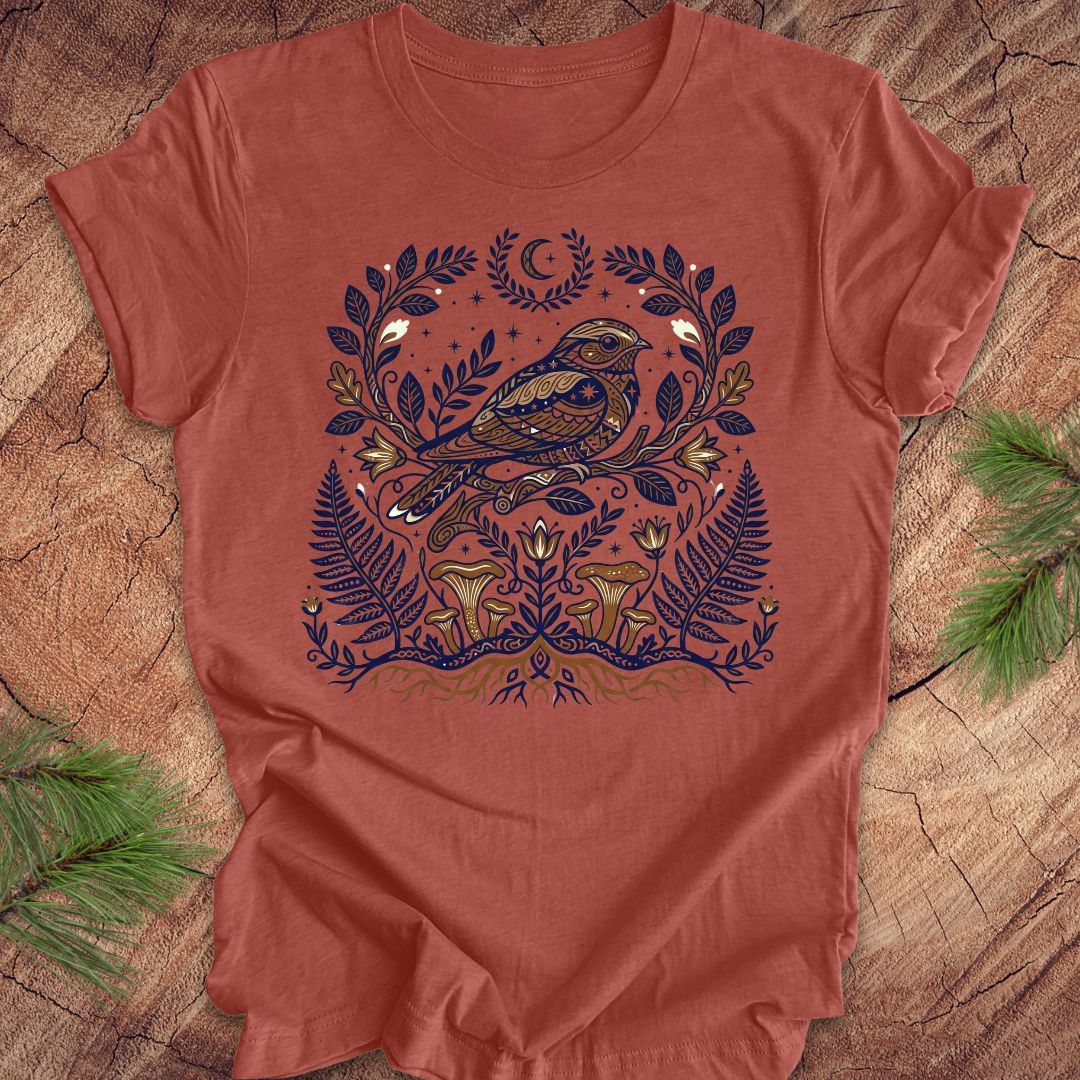 Clay colored t-shirt with a whip-poor-will and nature-themed design on a wooden surface.