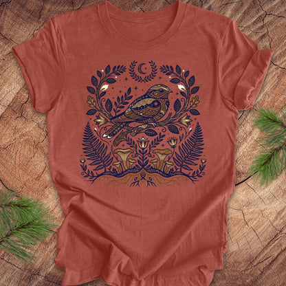 Clay colored t-shirt with a whip-poor-will and nature-themed design on a wooden surface.