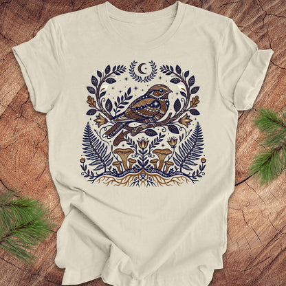 Beige t-shirt with a whip-poor-will and nature-themed design on a wooden surface.