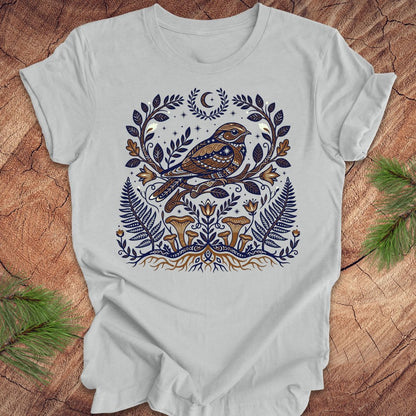 Silver t-shirt with a whip-poor-will and nature-themed design on a wooden surface.