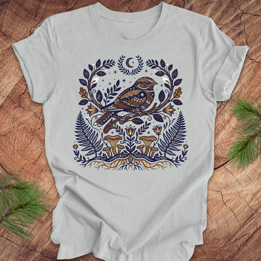 Silver t-shirt with a whip-poor-will and nature-themed design on a wooden surface.