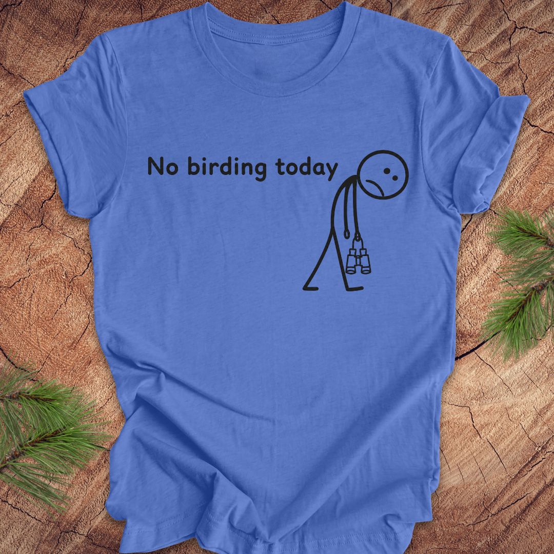 A blue short-sleeve crewneck t-shirt with a black graphic print that reads 'No birding today' above a simple stick figure holding binoculars, laid flat on a rustic wood surface with pine branches in the corners.
