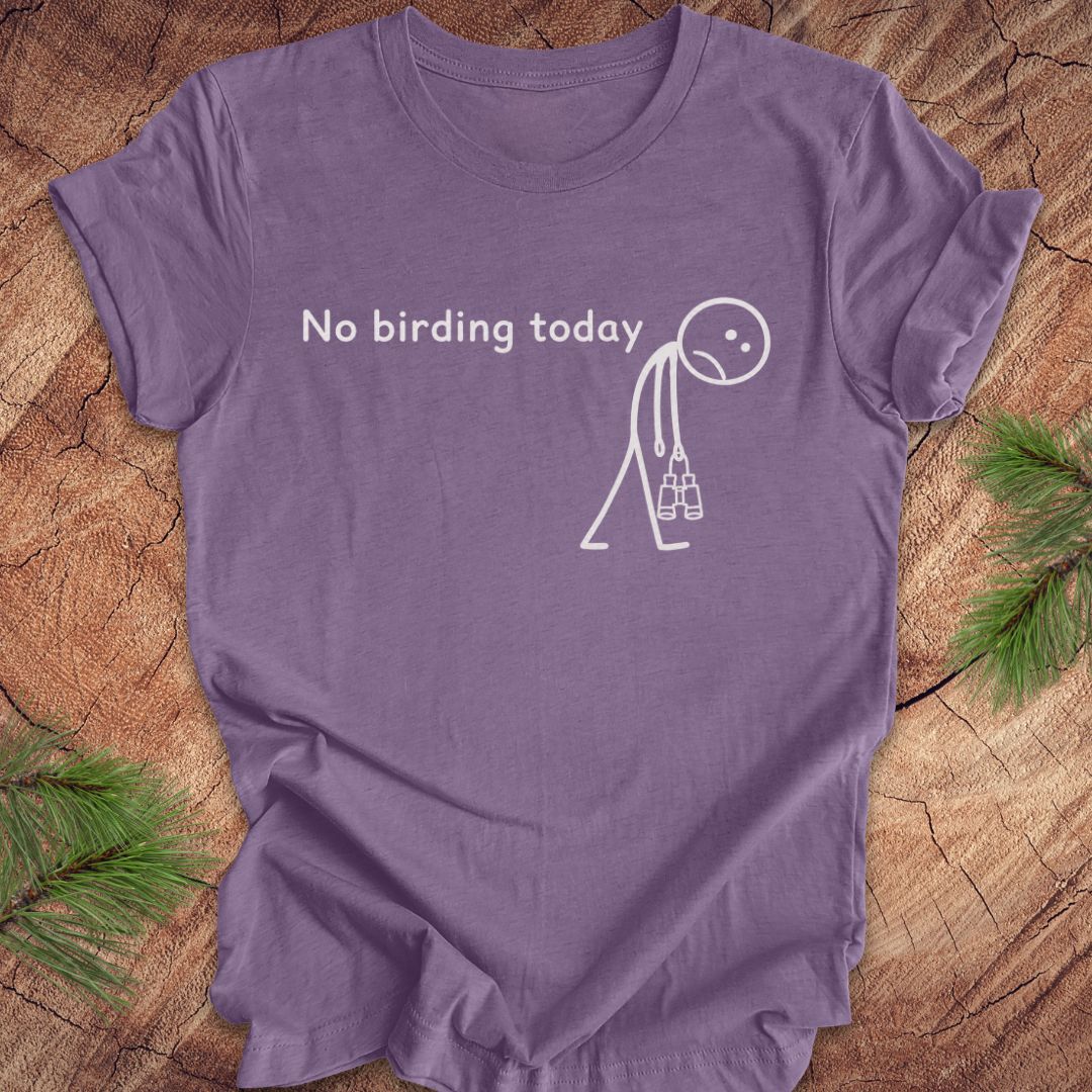 A purple short-sleeve t-shirt laid flat on a rustic wood surface with pine branches at the corners. The shirt has a white graphic print that reads 'No birding today' above a simple stick-figure style birding silhouette holding binoculars.