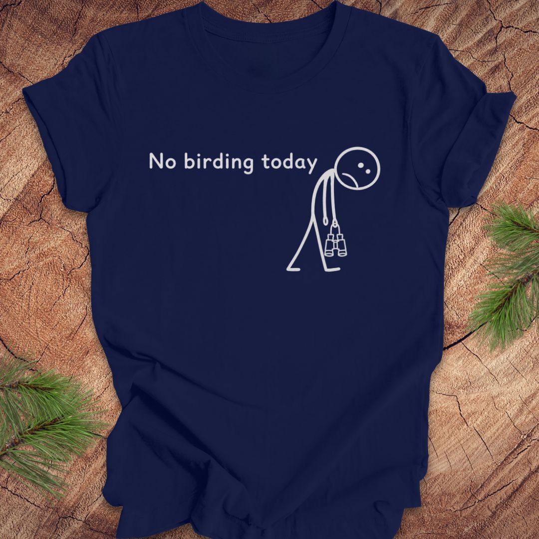 A navy blue short-sleeve t-shirt with a white graphic print that reads 'No birding today' next to a stick figure holding binoculars, displayed flat on a rustic wood background with pine needles in the corners.