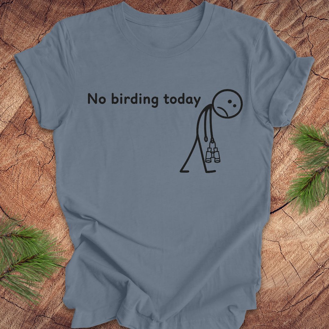 A slate blue crewneck t-shirt with a black graphic print that reads 'No birding today' next to a stick figure holding binoculars, displayed flat on a rustic wood background with pine needles.