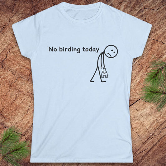 A light blue short-sleeve t-shirt with a black graphic print that reads 'No birding today' next to a stick figure holding binoculars, displayed flat on a rustic wood background with pine needles in the corners.
